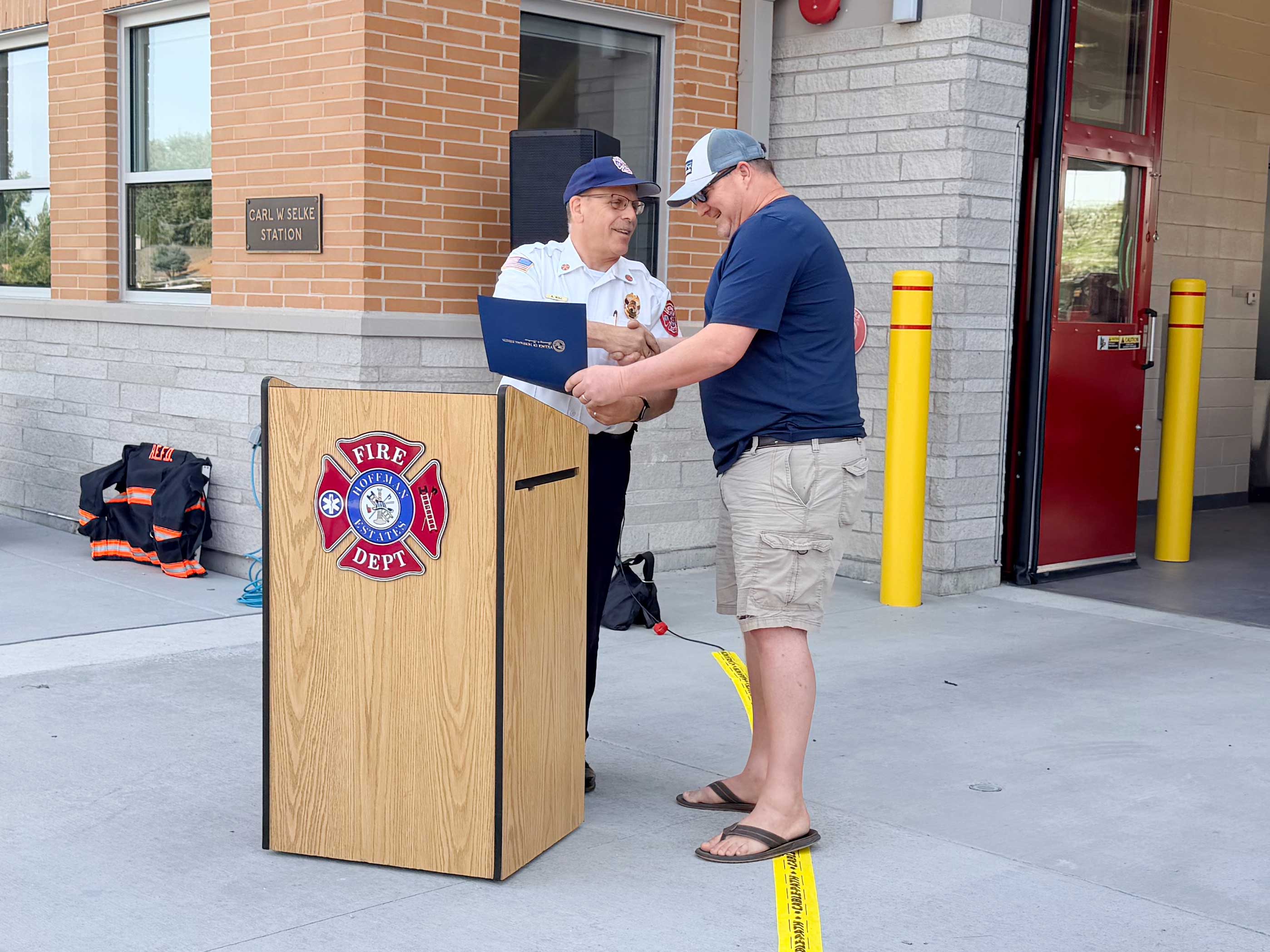 two men shaking hands standing near a podium adorned with the Hoffman Estates Fire Department logo